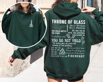 May include: Green hooded sweatshirt with a white graphic print of a sword and flames. The text reads "Throne of Glass", "You could rattle the stars to whatever end", "You do not yield", "The world will be saved and remade by the dreamers", "She was the heir of fire and ash and she would bow to no one Fireheart", "Hello, Witchling", "Hello, Princeeling", "We are the 13 until the darkness claims us", "Libraries were full of ideas. Perhaps the most dangerous and powerful of all weapons."