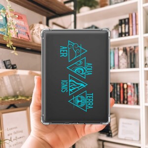 Op de afbeelding: Een zwarte tablet hoes met een turquoise afbeelding van de vier elementen: lucht, water, vuur en aarde. De hoes wordt in een hand gehouden, met een boekenplank op de achtergrond. De tekst op de hoes luidt "AER", "AQUA", "IGNIS" en "TERRA".