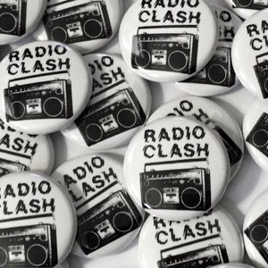May include: A collection of white round buttons with black and white images of a boombox and the text "Radio Clash".