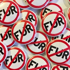 May include: A collection of white buttons with a red border and the words "FUR" in black, crossed out with a red diagonal line. The buttons are scattered across a white surface.