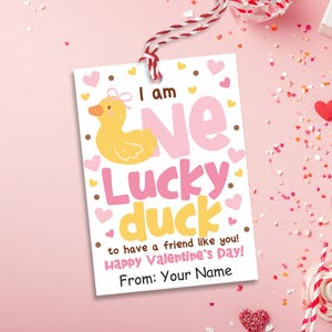 May include: A Valentine's Day gift tag with a yellow duck illustration and the words "I am one lucky duck" in pink and yellow. The tag has a red and white string and is decorated with hearts.