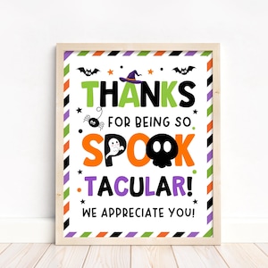 Op de afbeelding: Een ingelijst rechthoekig bord met een witte achtergrond en een gestreepte rand in groen, oranje, paars en zwart. De tekst luidt THANKS FOR BEING SO SPOOK-TACULAR! WE APPRECIATE YOU! met illustraties van een heksenhoed, vleermuizen, een spin en een geest.