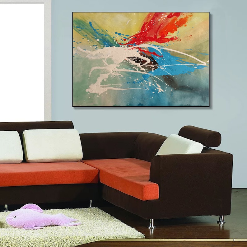 May include: Abstract painting with splashes of red, blue, green, and white paint on a yellow background. The painting is hanging on a wall above a brown sectional sofa.