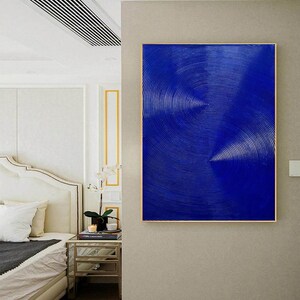 May include: Abstract painting with a blue background and white lines creating a swirling pattern. The painting is framed in a gold frame and is hanging on a wall.