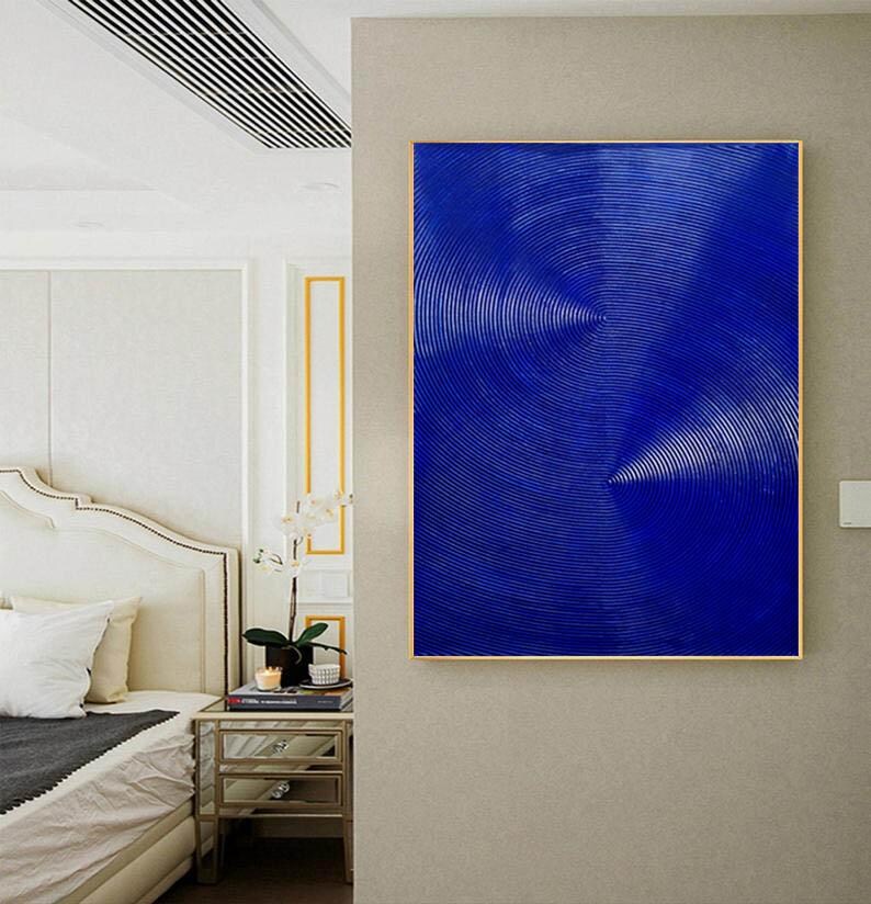 May include: Abstract painting with a blue background and white lines creating a swirling pattern. The painting is framed in a gold frame and is hanging on a wall.