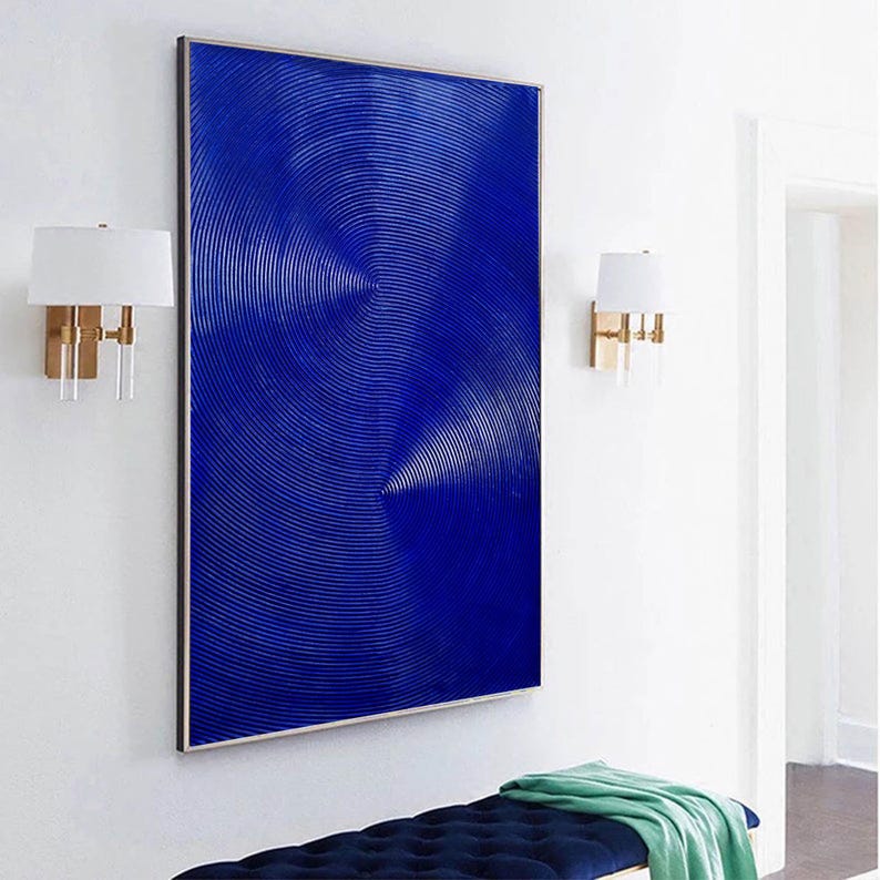 May include: A large abstract painting with a blue background and a pattern of concentric circles. The painting is framed in a silver frame and is hanging on a white wall.