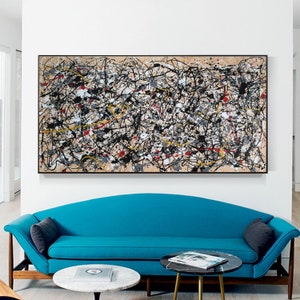 May include: Abstract painting with black, white, yellow, and red paint splatters on a beige background. The painting is framed in black and hanging on a white wall above a blue sofa.