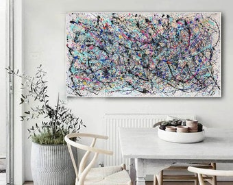 May include: Abstract painting with black, blue, white, and pink paint splatters and lines on a white canvas. The painting is hanging on a white wall in a room with a white table and chairs.