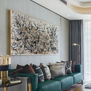 May include: A large abstract painting in black and white with a gold frame hangs above a green sofa with brown and white patterned throw pillows.