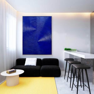 May include: A modern living room interior with a black sectional sofa, a white coffee table, and a yellow rug. A large abstract painting with white lines on a blue background hangs on the wall. Three black bar stools are in the background.