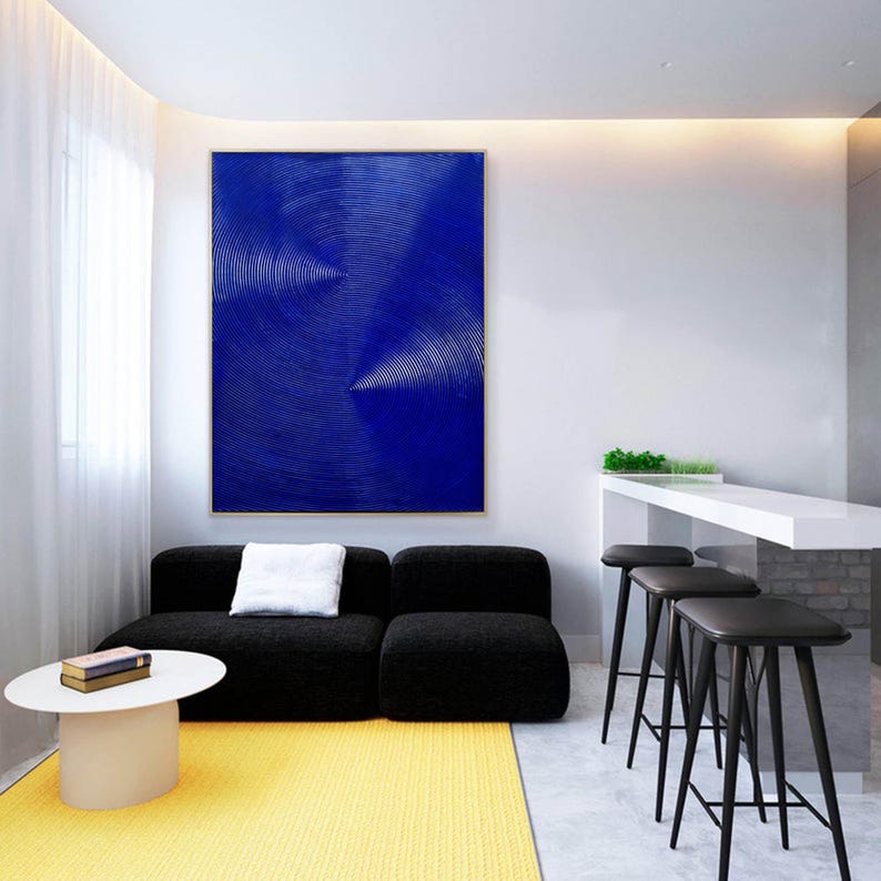 May include: A modern living room interior with a black sectional sofa, a white coffee table, and a yellow rug. A large abstract painting with white lines on a blue background hangs on the wall. Three black bar stools are in the background.