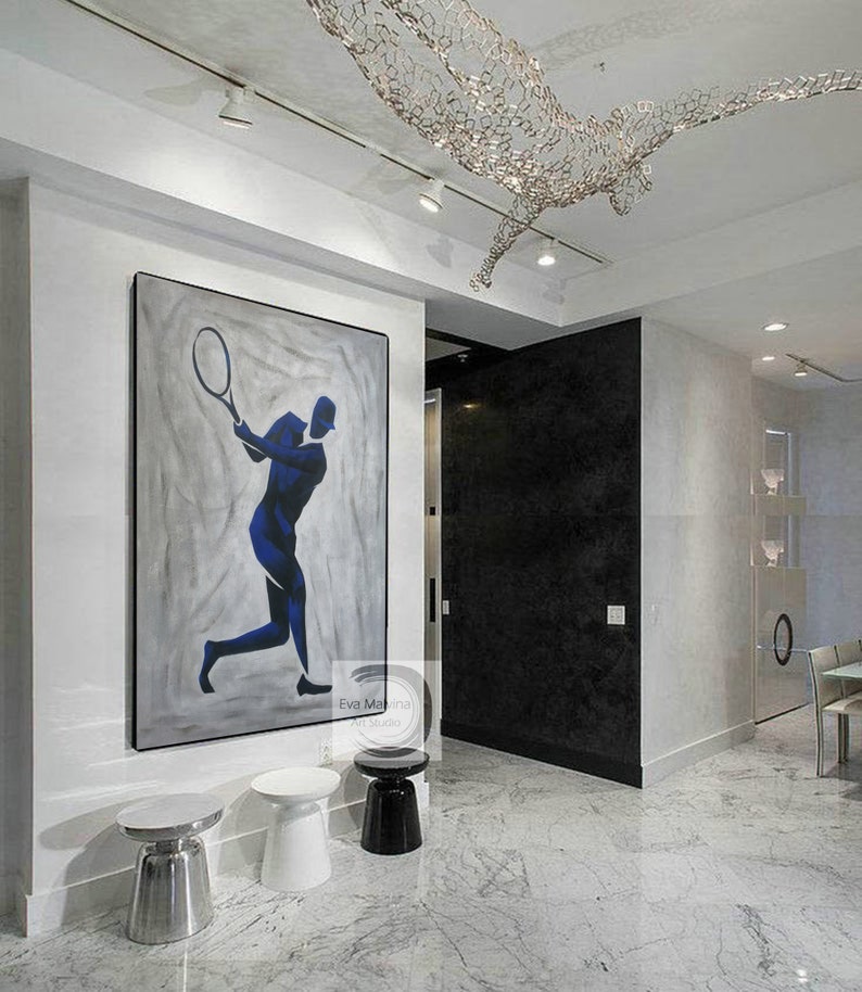 K&ouml;nnte beinhalten: Ein modernes Innendesign mit einem gro&szlig;en abstrakten Gem&auml;lde eines Tennisspielers in Blau und Wei&szlig; auf grauem Hintergrund. Das Gem&auml;lde h&auml;ngt an einer wei&szlig;en Wand mit drei silbernen und schwarzen Beistelltischen. Der Raum hat einen wei&szlig;en Marmorboden und eine schwarze Wand mit einer T&uuml;r, die zu einem anderen Raum f&uuml;hrt.