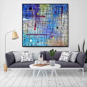May include: Abstract painting with a blue background and black, white, red, and yellow lines. The painting is framed in black and hanging on a white wall above a gray couch with pillows.