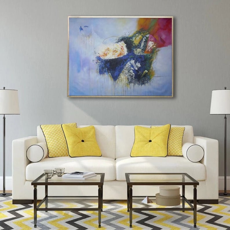 May include: A white couch with yellow throw pillows sits in front of a gray wall with an abstract painting above it. The painting features blue, white, and red colors with a textured, brushstroke effect.
