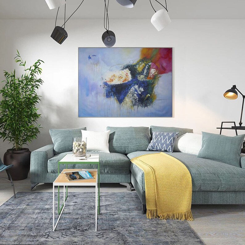 May include: A blue sectional sofa with a yellow throw blanket and a white coffee table with a green trim. The sofa is in a living room with a large abstract painting on the wall and a potted plant in the corner.