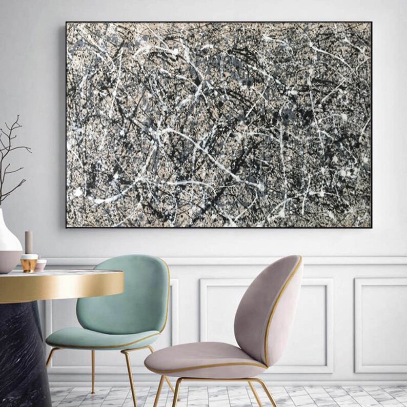 May include: Abstract painting with black, white and grey paint splatters and lines on a beige background. The painting is framed in black and hanging on a white wall.