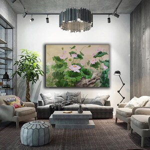 May include: A painting of pink lotus flowers with green leaves and a brown branch in the background. The painting is framed and hanging on a white wall in a living room setting.