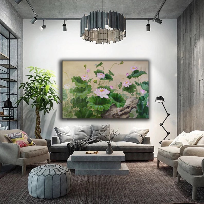 May include: A painting of pink lotus flowers with green leaves and a brown branch in the background. The painting is framed and hanging on a white wall in a living room setting.