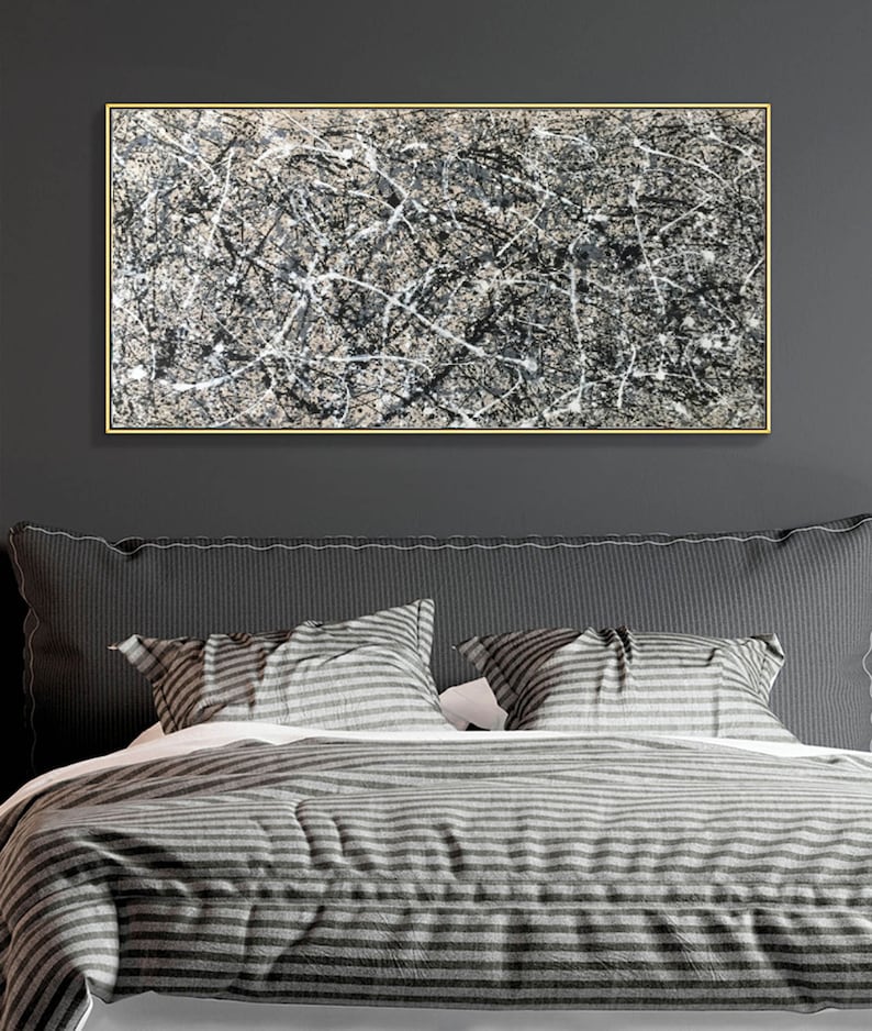 May include: Abstract black and white painting in a gold frame hanging above a grey striped bed with two pillows.