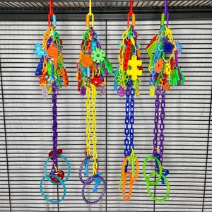 May include: Four colorful bird toys hanging from a metal cage. Each toy features a chain, plastic rings, and a variety of brightly colored plastic shapes and beads. The toys are in shades of red, yellow, blue, green, and purple.
