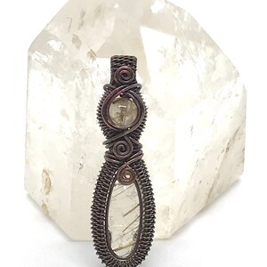 May include: A wire-wrapped pendant featuring a clear quartz crystal with gold inclusions. The pendant is made with copper wire and has a rustic, antique finish.