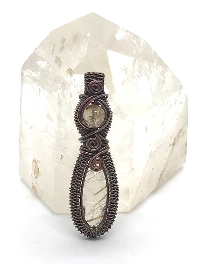 May include: A wire-wrapped pendant featuring a clear quartz crystal with gold inclusions. The pendant is made with copper wire and has a rustic, antique finish.