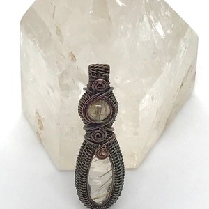 May include: A wire-wrapped pendant featuring two clear quartz stones with gold inclusions. The pendant is made with copper wire and has a rustic, antique finish.