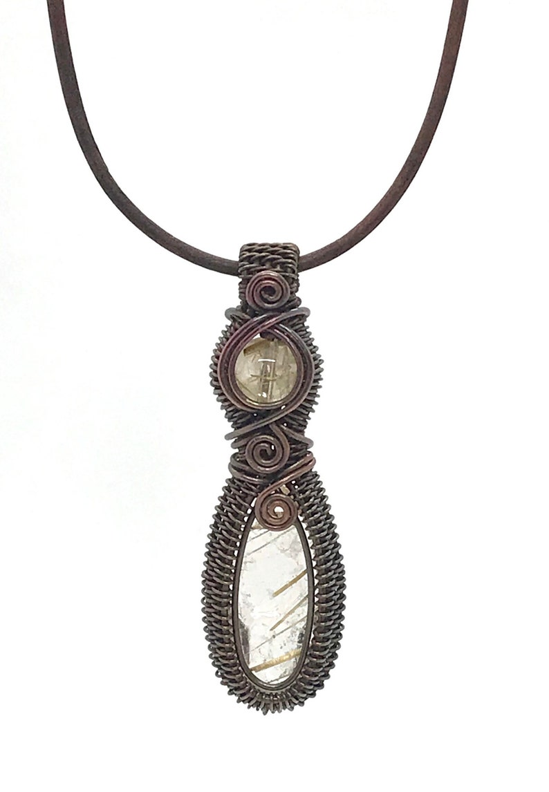 May include: A copper wire wrapped pendant necklace featuring a clear quartz crystal with gold inclusions. The pendant is suspended from a brown leather cord.