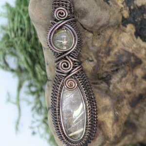 May include: A wire-wrapped pendant featuring a clear quartz crystal with gold inclusions. The pendant is made with copper wire and has a woven design.
