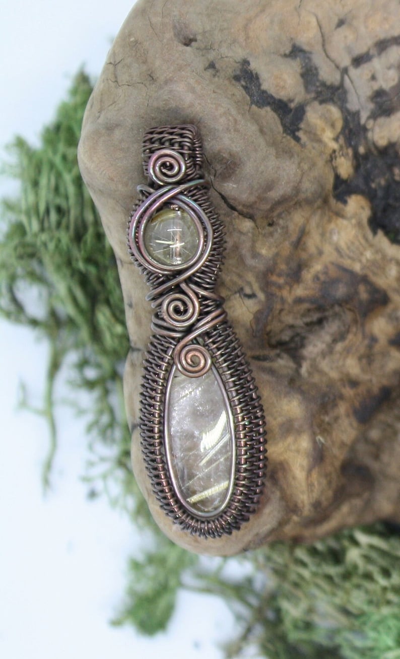 May include: A wire-wrapped pendant featuring a clear quartz crystal with gold inclusions. The pendant is made with copper wire and has a woven design.