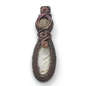 May include: A wire-wrapped pendant featuring a clear quartz crystal with gold inclusions. The pendant is made with copper wire and has a brown and iridescent finish.