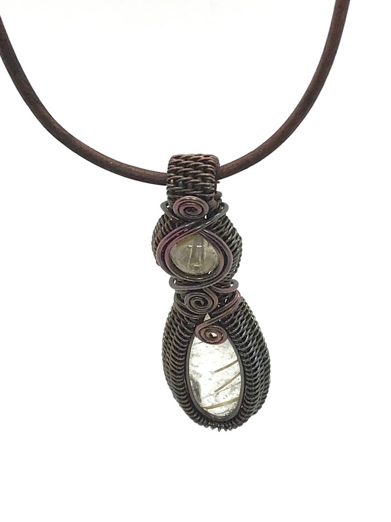 May include: A copper wire wrapped pendant necklace with a clear quartz stone. The pendant is in the shape of a teardrop and has a brown leather cord.