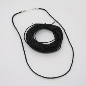 以下が含まれることがあります： 銀色の留め具が片側に付いた、黒いワックスコードの糸巻き。コードは円形に巻かれており、ジュエリー作りやその他のクラフトに使うことができます。