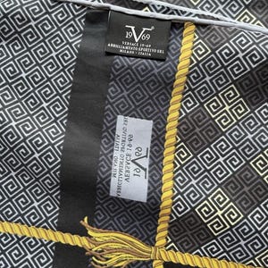 Peut inclure: Un foulard noir et blanc &agrave; motifs avec des accents de corde et de glands dor&eacute;s. Le foulard pr&eacute;sente un motif g&eacute;om&eacute;trique r&eacute;p&eacute;titif et la marque "Versace 19-69" est visible sur une &eacute;tiquette.