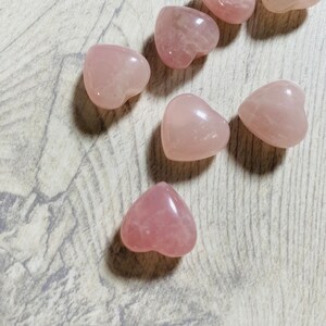 May include: Seven pink heart-shaped rose quartz crystals on a light wood background.