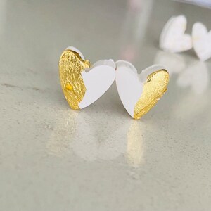 May include: A pair of white heart-shaped earrings with gold leaf accents.
