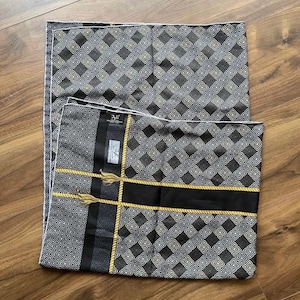 Peut inclure: Deux coussins d&eacute;coratifs noirs et gris &agrave; motifs g&eacute;om&eacute;triques. Un coussin a une bande noire avec une bordure en corde dor&eacute;e et des glands. Les coussins ont une bordure blanche et sont sur une surface en bois.