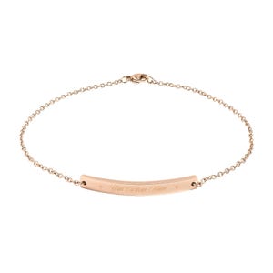 May include: Rose gold bracelet with a delicate chain and a curved bar. The bar is engraved with the text "Your Custom Name" and has a small star on each end. A simple and elegant piece of jewelry.