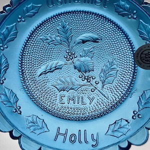 May include: A blue glass plate with a holly leaf and berry design. The plate has a scalloped edge and the name "Emily" and "Holly" are inscribed. The plate has a textured surface and is likely vintage.