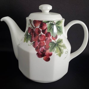 May include: White porcelain teapot with a grapevine and grapes design. The teapot has a lid and a handle.