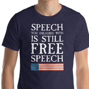 May include: A navy blue t-shirt with white text that reads "Speech you disagree with is still free speech" and a small American flag graphic.