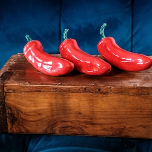 May include: Three red chilli peppers on a wooden box. The peppers are glossy and have green stems.