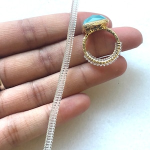 May include: A gold ring with a light blue gemstone and a clear plastic ring sizer.