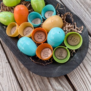 May include: A black bowl filled with plastic Easter eggs, each containing a different prize. The prizes include: "Movie", "Craft Project", "Play at the Park", "Have a Friend Over", "£1", "1 Hour Extra Screen Time", "Go Get Ice Cream", and "£10".