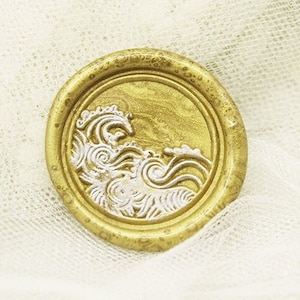 May include: A gold wax seal with a white wave design. The seal is on a white background.