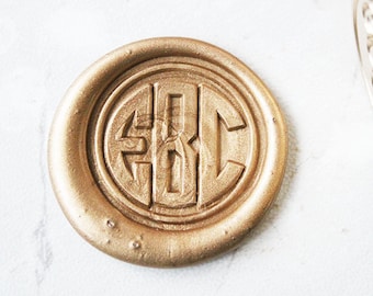 Könnte beinhalten: Ein goldenes Siegelwachs mit den Initialen "EBC" im Zentrum geprägt. Das Siegel befindet sich auf einer weißen Oberfläche.