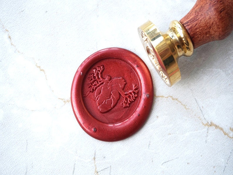 May include: A red wax seal with a detailed anatomical heart design. The seal is made with a traditional wax seal stamp.