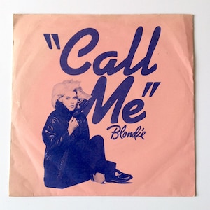 May include: A pink record sleeve with a blue and white image of a woman in a leather jacket and the text "Call Me" in blue with "Blondie" in smaller blue text below.