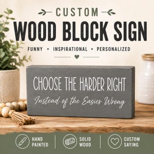 May include: A rectangular dark gray wood block sign featuring white text that reads CHOOSE THE HARDER RIGHT Instead of the Easier Wrong. The sign is displayed on a wooden surface with decorative wooden beads and a small tassel visible nearby.