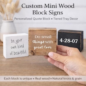 May include: Three rectangular wooden block signs featuring text. One white block reads 'be your own kind of beautiful', one natural wood block reads 'Do small things with great love', and one black block displays the date '4-28-07' in white text.